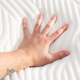 A hand pressing into the surface of a mattress