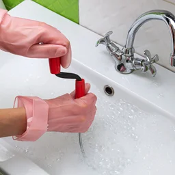 Person wearing pink rubber gloves uses drain snake on blocked sink